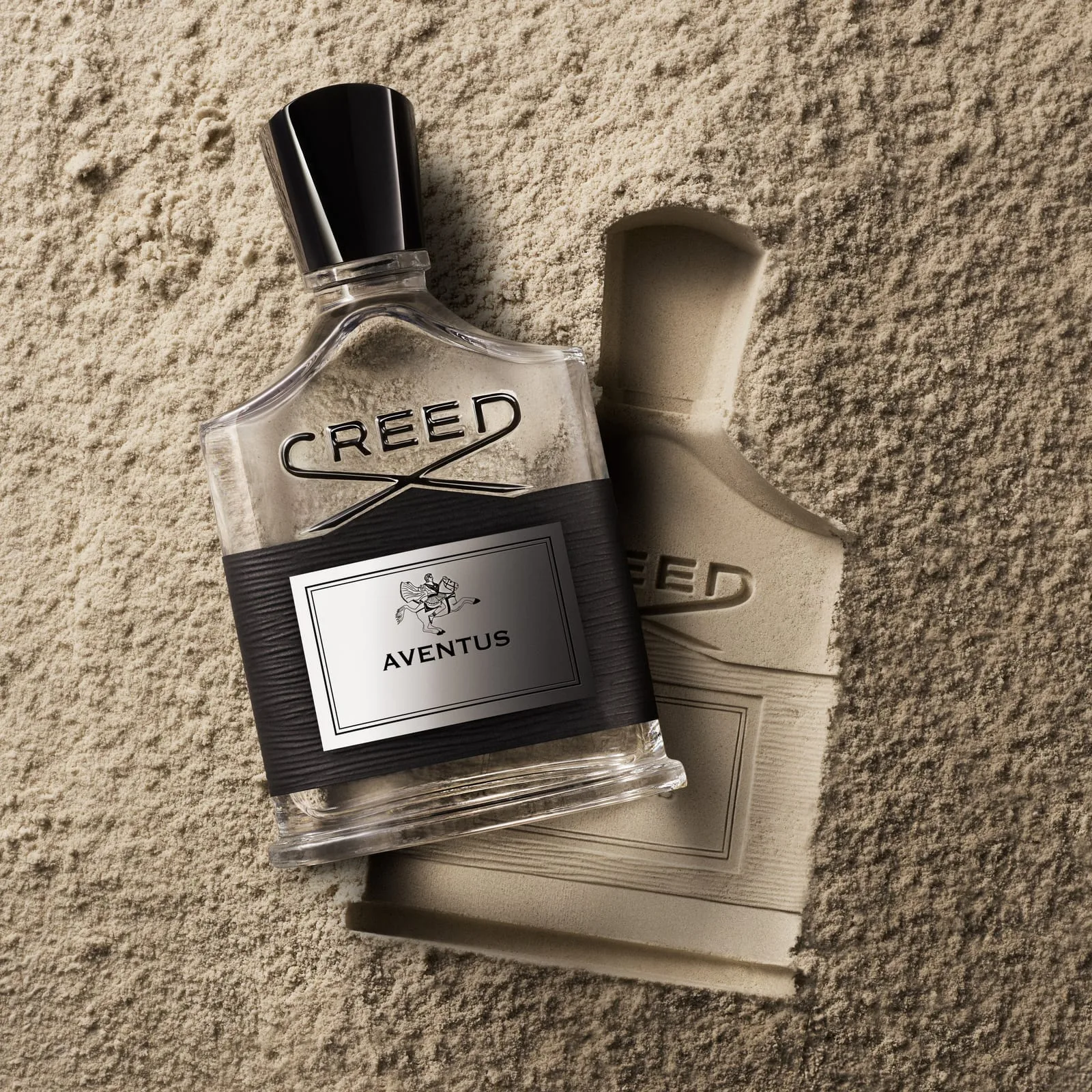 The Aventus bottle lies at rest beside the impression it has left in a bed of pale stone dust — object and imprint
