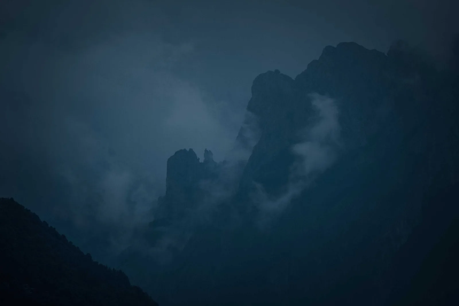 Black crags at nightfall in blue-grey gloom, ribbons of cloud smoking off the ridgeline like birch fires burning somewhere far below