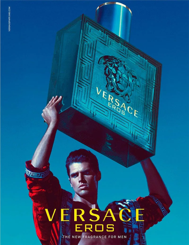 Robed in red Baroque silk, the model hoists the monumental turquoise flacon overhead like an offering to the sky