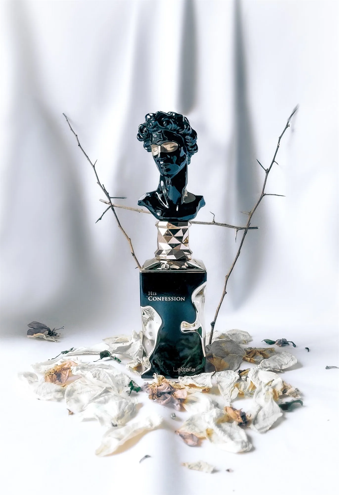 The black bust bottle on white drapery among dried rose petals and thorn branches