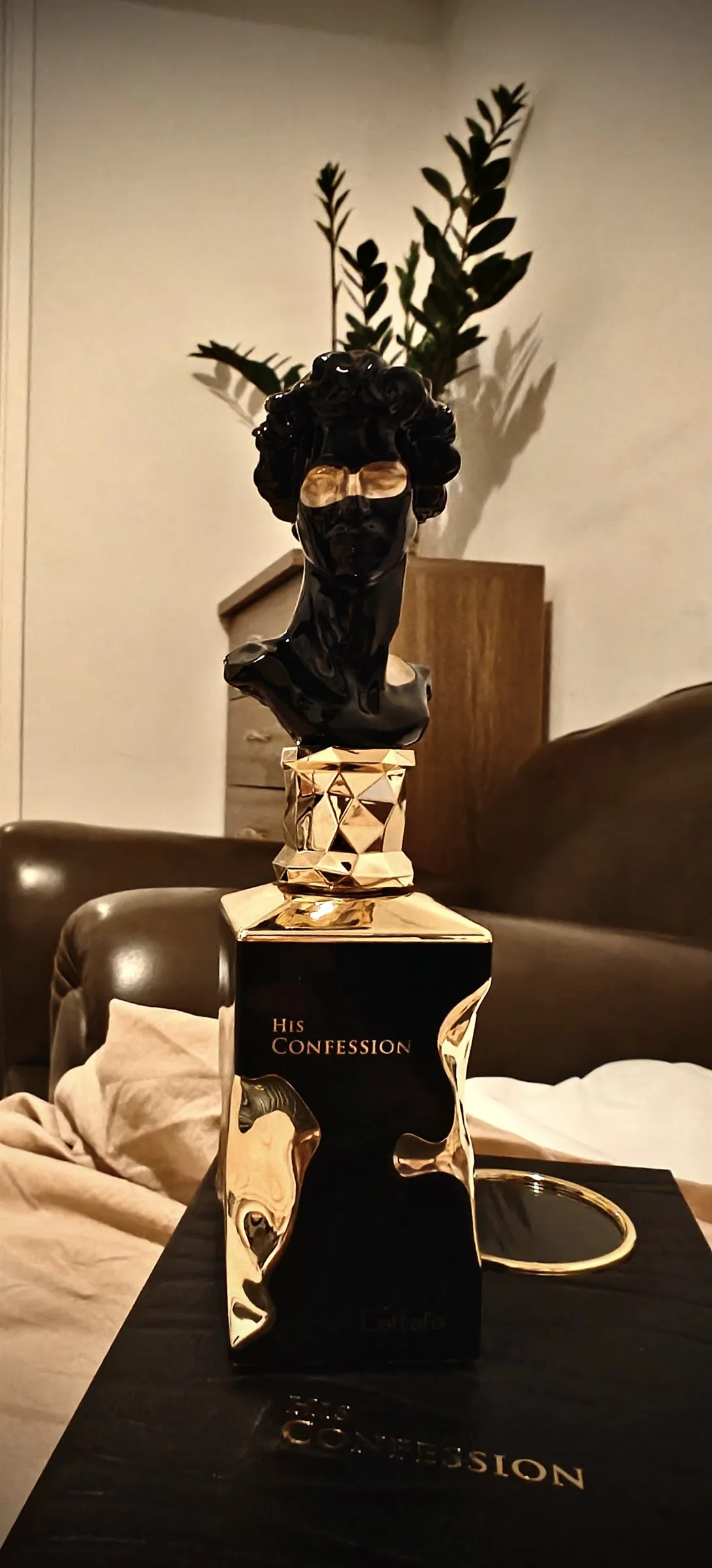 The bottle on a dark table by lamplight, a green plant and leather sofa behind