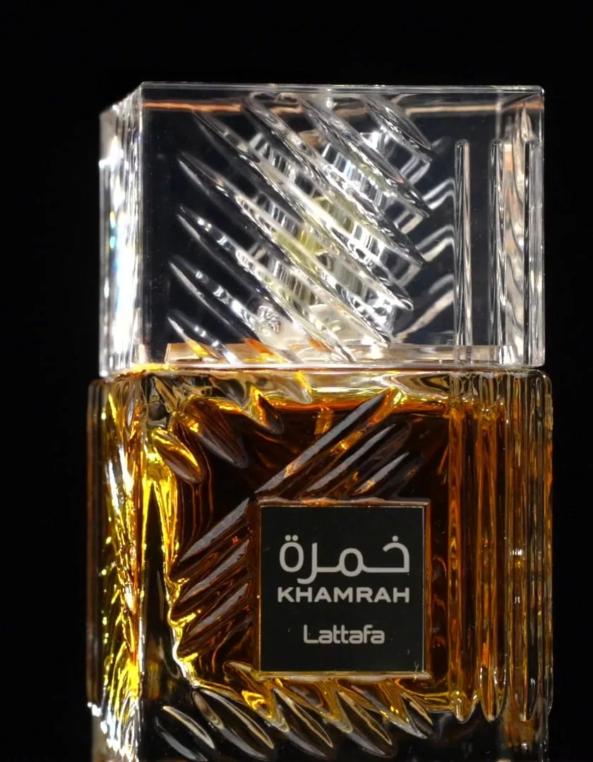 The cut-glass tumbler bottle alone against pure black, its amber liquid lit from within like whisky by candlelight, a faint reflection pooling beneath it