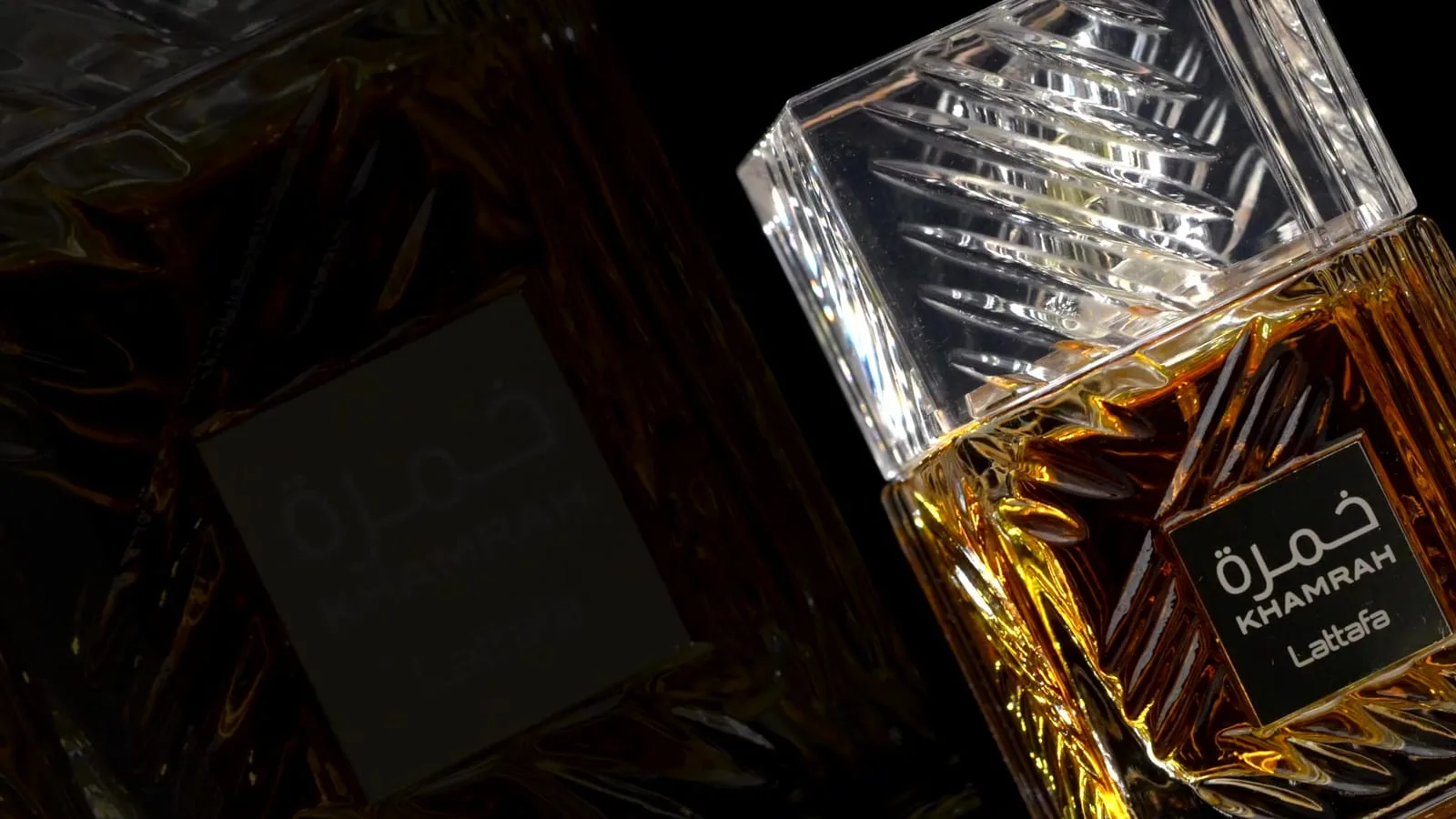 Two faceted bottles lean through the dark on a diagonal, one sunk in shadow, the other blazing amber and gold where the light catches the cut glass