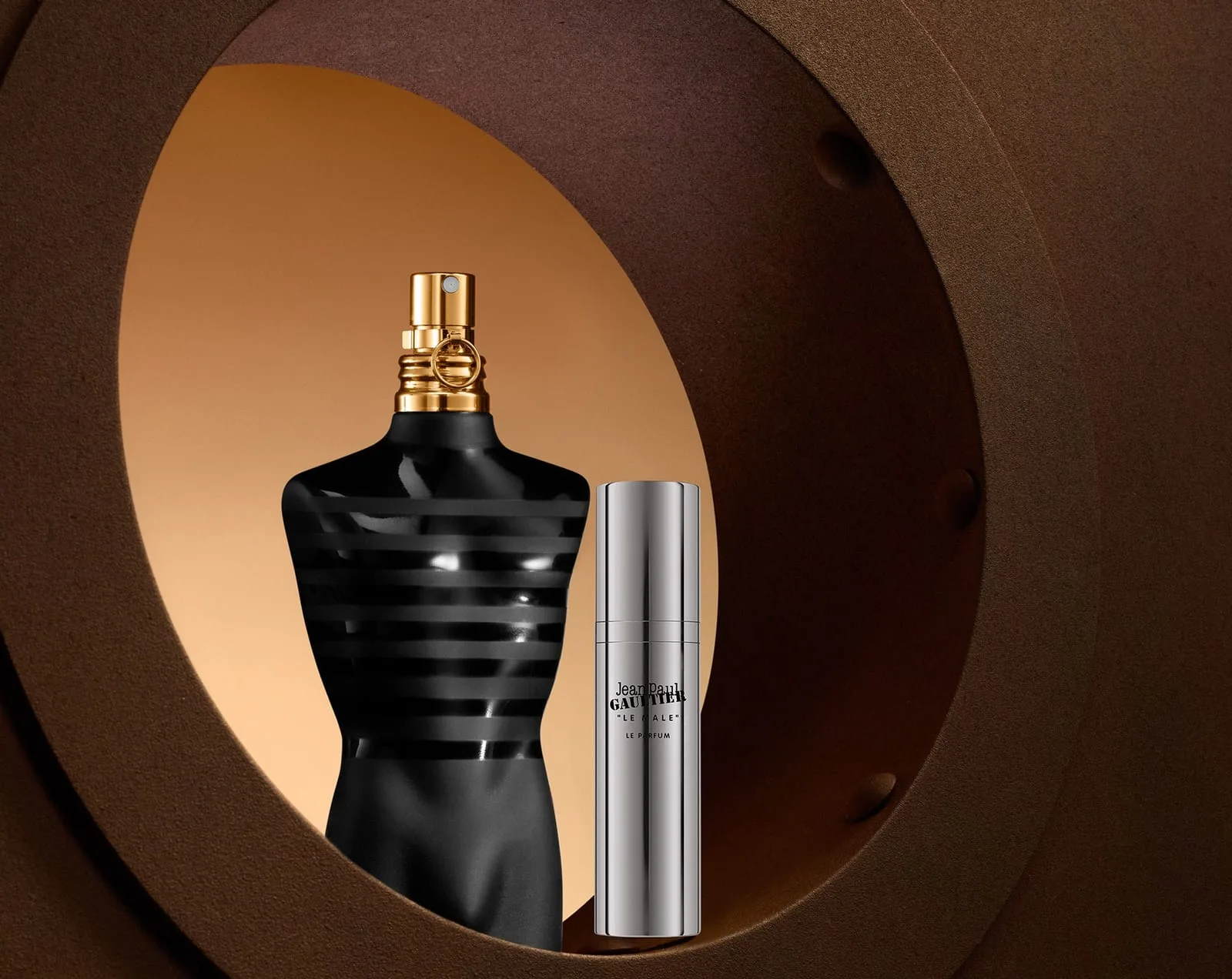The matte-black striped torso bottle with its gilded collar stands in the amber glow of a ship's porthole, a silver travel spray at its side