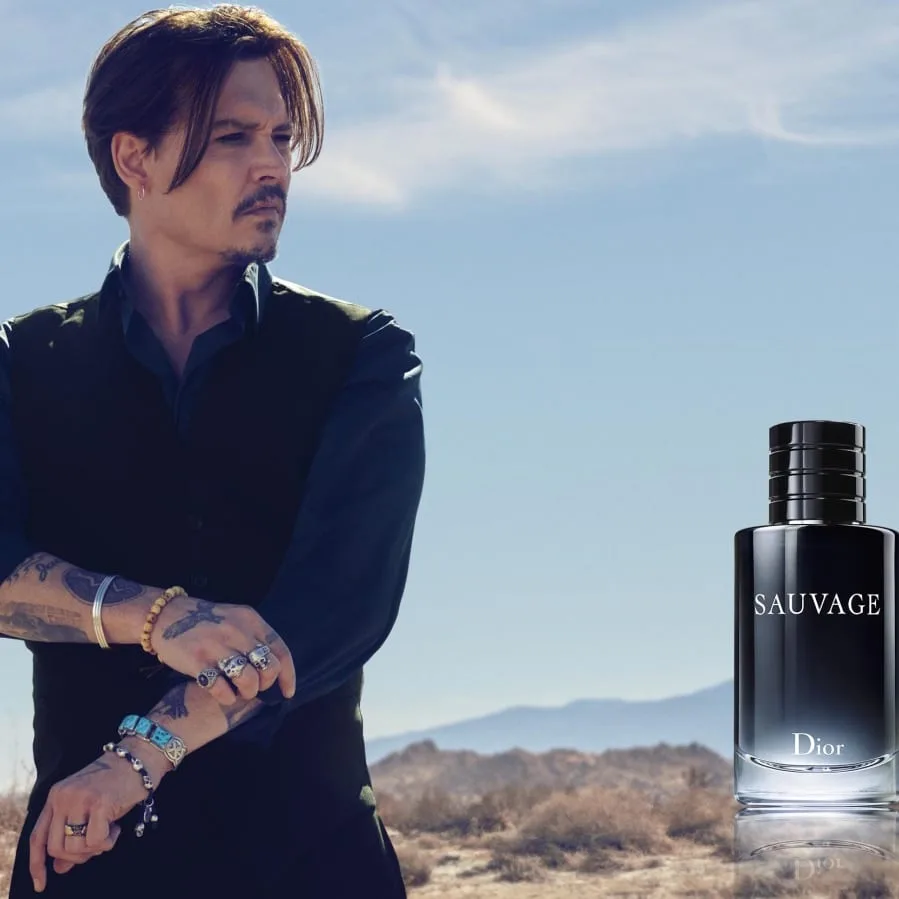 Depp rolls up a sleeve under an ozone-blue desert sky, rings and turquoise at his wrists, while the dark Sauvage flacon stands monumental against the scrubland